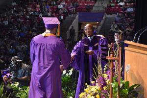 man hands graduate his diploma during commencement