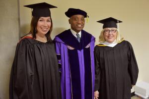 two females and man in black cap and gowns at commencement