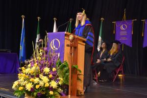 woman standing at podium wearing black and blue cap and gown
