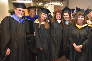 faculty in black cap and gowns smile in a group