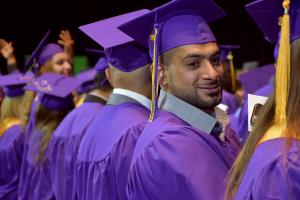 man with puprle cap and gown smiles at commencement
