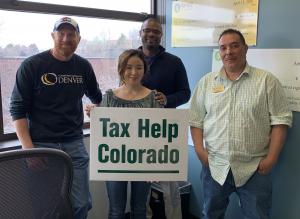 student and her professors standing together, smiling and holding a sign that says Tax Help Colorado