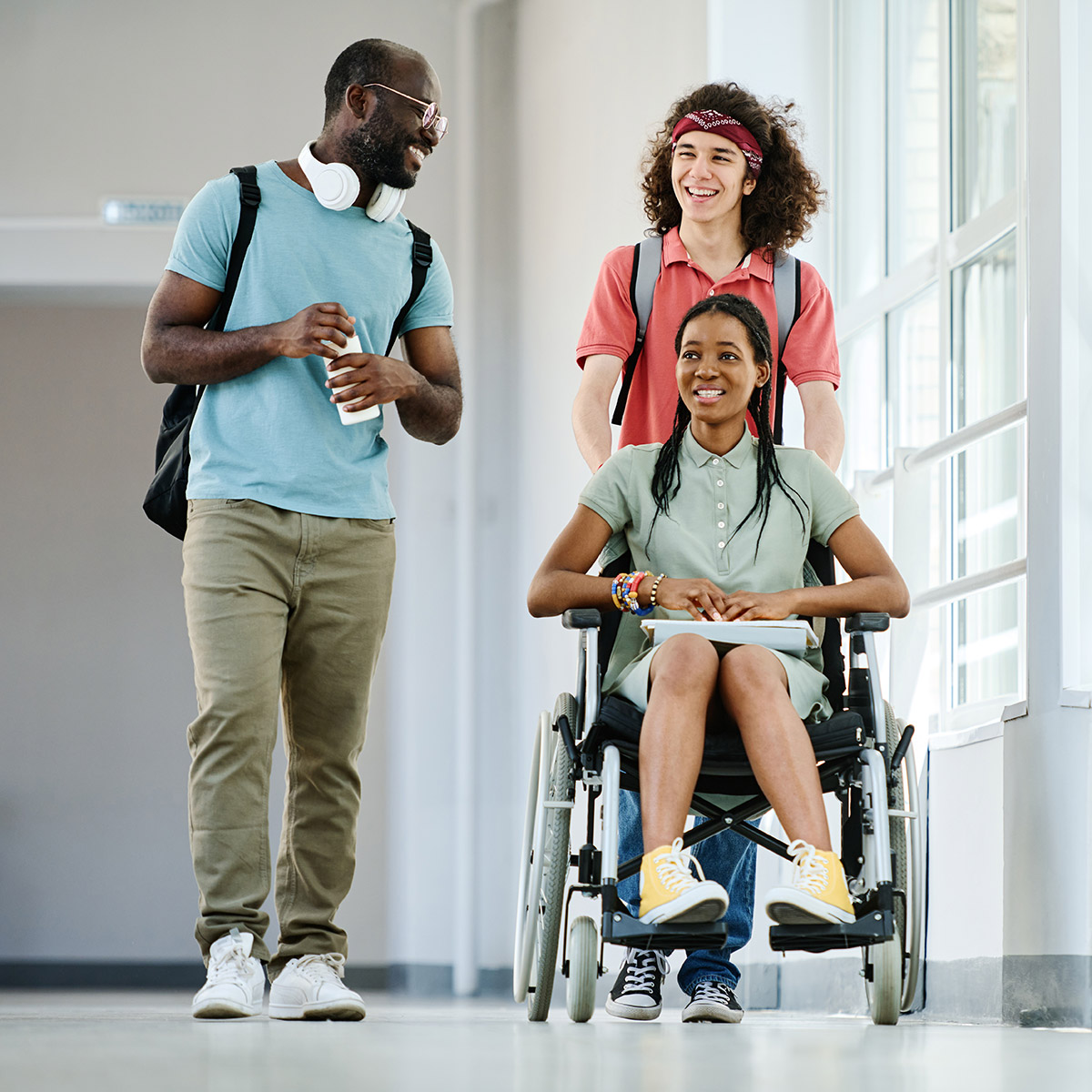2 male CCD students walking alongside a female student in a wheelchair