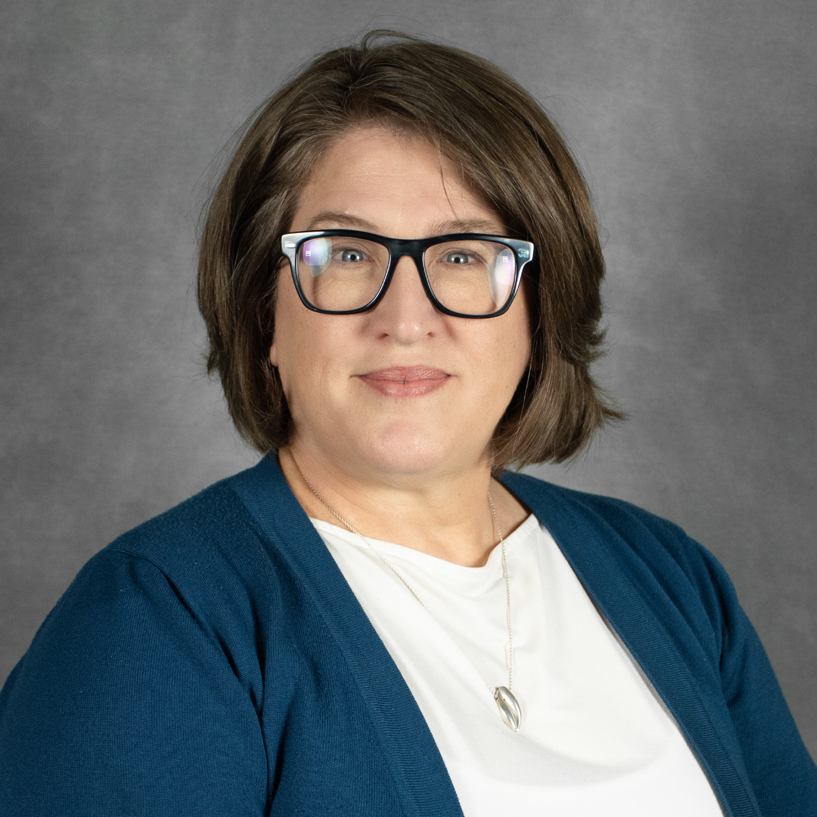 woman with brown bob wearing black glasses, white shirt and blue sweater