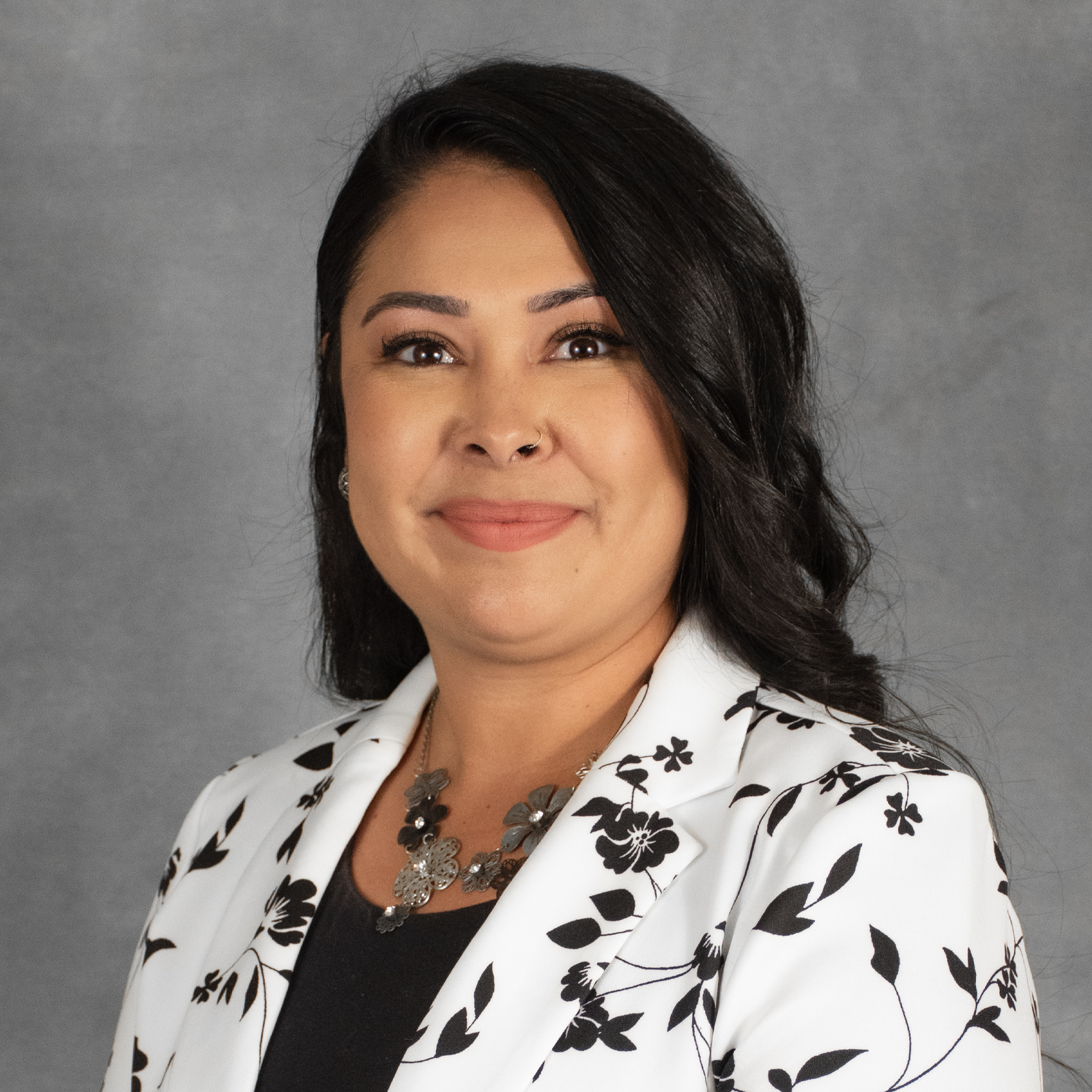 Woman with long dark hair wearing black and white flowered blazer