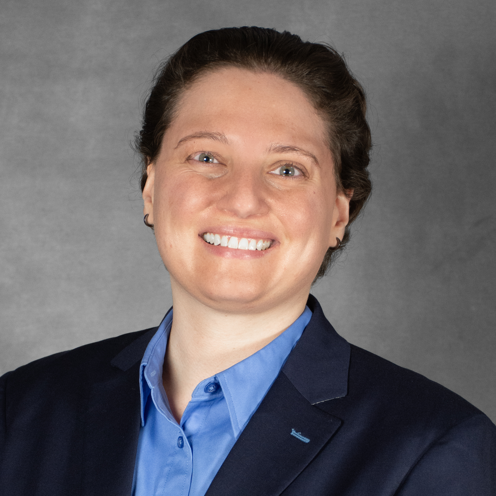 Person with short brown hair wearing a blue collared shirt and navy blazer