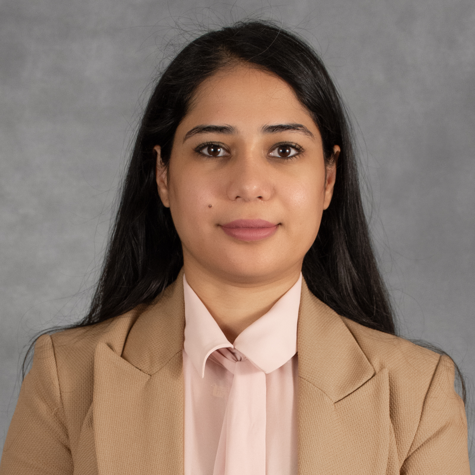 Woman with long black hair wearing a tan blazer and pink shirt