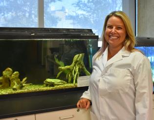 white woman standing in a lab in front of a fish tank smiling