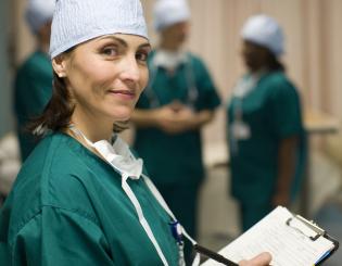A young nurse wearing green medical scrubs holding a clipboard.