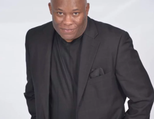 black man in a black jacket standing smiling with his hands in his pockets