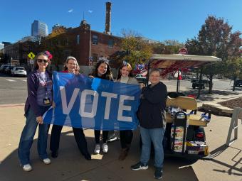 People holding a blue "Vote" flag outside.