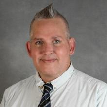 man with short grayish hair in a spike wearing white shirt and striped tie