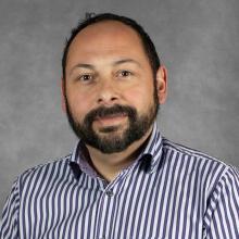 Man with short brown hair and beard wearing striped shirt