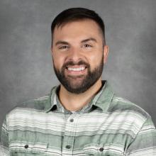 man with short dark hair an beard wearing green striped shirt