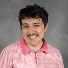 man with dark curly hair wearing pink striped polo