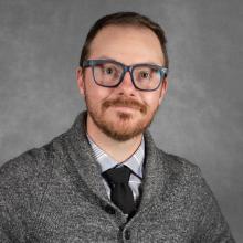 man with reddish short hair and beard wearing black tie and gray sweater