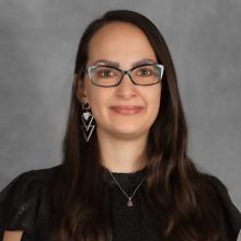 Woman with long dark hair wearing a black top and ornate earrings