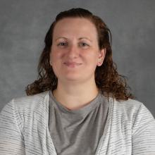 Woman with medium length reddish hair wearing gray top and white sweater