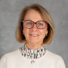 Woman with short blond bob wearing red glasses, white sweater and print turtleneck