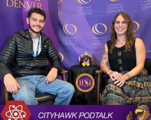 Man with facial hair in black jacket sitting next to a woman with brown hair wearing a patterned dress. CITYHAWK PODTALK.