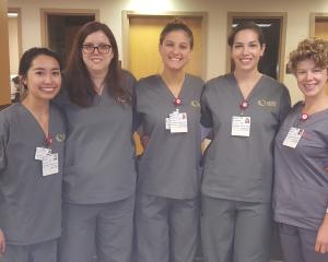 5 young nurse aide students standing in scrubs smiling