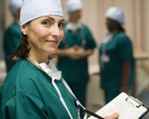 A young nurse wearing green medical scrubs holding a clipboard.